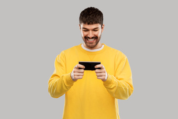 technology, communication and people concept - happy smiling young man playing game on smartphone over grey background