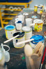 Table of artist or painter with multiple jars with colorful paint. Accessories and tools for creative work. Workshop or workplace setting