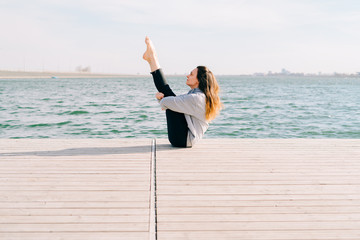 a young beautiful stylish girl is sitting on a pier near the lake on a Sunny spring day