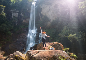 Young woman traveler is having fun on summer vacation on background waterfall