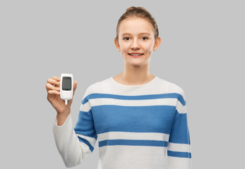 health, medicine and diabetic concept - happy smiling teenage girl with glucometer over grey...