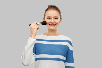 beauty, cosmetics and people concept - happy smiling teenage girl in pullover with make up brush over grey background