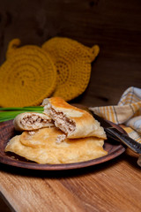 Clay plate of fried meat pies with cutlery and green onion on wooden table.