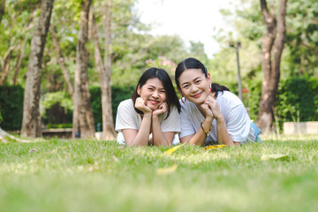 Young asian girl friends lying down in grass looking to camera and smiling.