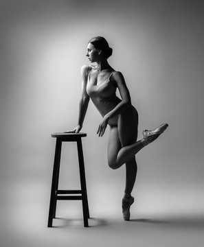 Ballerina in gray outfit posing on cheir, studio background. Grayscale image.