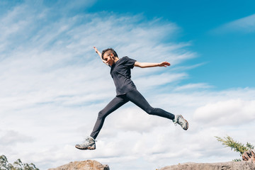 Obraz premium Young girl jumping between the rocks in a mountain race. She is training. blue sky background. Concept of healthy life and sports.