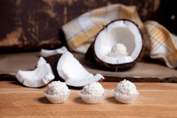 Coconut with white pulp and white candies on wooden background..