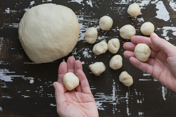 Small balls of dough in woman hands before roll it for making vareniki on brown background