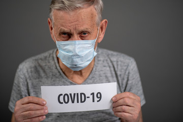 Man with a sign. Old man, 80 years old, in a medical protective mask. He is holding a white sheet of paper with the inscription covid19.