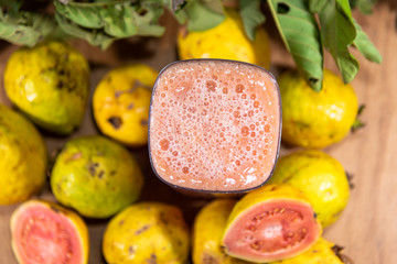 Glass of guava juice around fresh fruits and guava leaves
