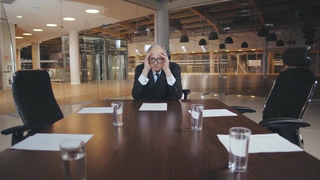 Tired elderly businessman sitting alone in conference room - Powered by Adobe