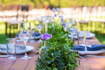 Beautifully decorated wooden table in a summer open-air cafe. Green branch and fresh flowers table decoration