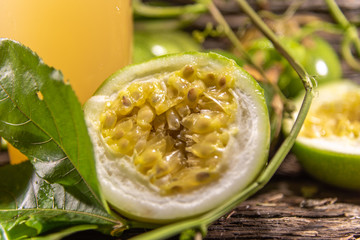 Glass of passion fruit juice among fresh broken fruits on a woody background