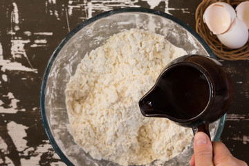 Woman hand holding ladle with hot water to put it into flour to make dough on brown background