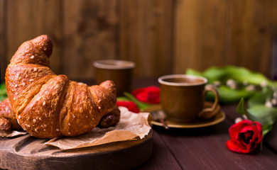 croissant and coffee. Fresh italian pastries and aromatic coffee on a wooden table and red tulips. Beautiful food postcard. Copy space.