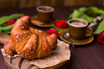 croissant and coffee. Fresh italian pastries and aromatic coffee on a wooden table and red tulips. Rustic style photo . Copy space