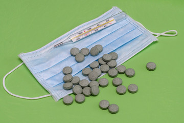 protective medical mask, thermometer and pills on a green background