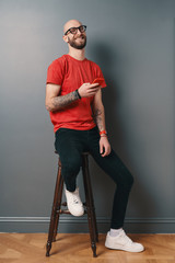 Fototapeta na wymiar Handsome hairless man with beard,texting while holding smartphone in his tattooed arm on gray studio background