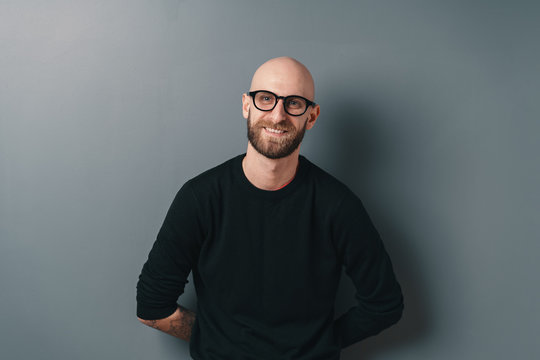 Young smiling man with beard and glasses on gray studio background