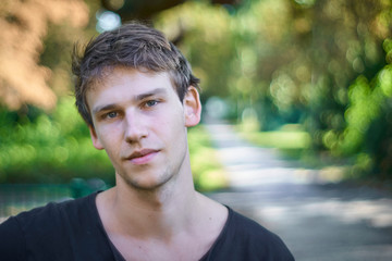 Portrait of a relaxed young man with a sympathetic confident look, dressed casually in a park in summer.