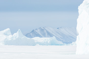 Ice berg on frozen sea in front of mountain, Greenland.