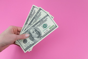 Girl holds money, American banknote on pink background. Concept of money, earning, taxes, paying twice.