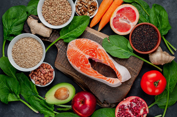 Selection of healthy food: salmon, fruits, seeds, cereals, superfoods, vegetables, leafy vegetables on a stone background. Healthy food for people.
