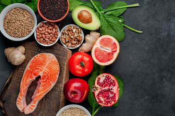 Selection of healthy food: salmon, fruits, seeds, cereals, superfoods, vegetables, leafy vegetables on a stone background  with copy space for your text. Healthy food for people.