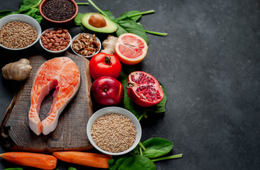 Selection of healthy food: salmon, fruits, seeds, cereals, superfoods, vegetables, leafy vegetables on a stone background  with copy space for your text. Healthy food for people.