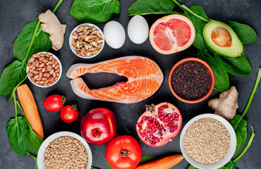 Selection of healthy food: salmon, fruits, seeds, cereals, superfoods, vegetables, leafy vegetables on a stone background. Healthy food for people.