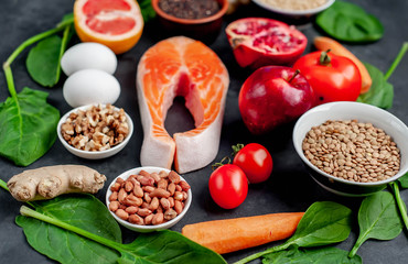 Selection of healthy food: salmon, fruits, seeds, cereals, superfoods, vegetables, leafy vegetables on a stone background. Healthy food for people.