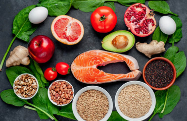 Selection of healthy food: salmon, fruits, seeds, cereals, superfoods, vegetables, leafy vegetables on a stone background. Healthy food for people.