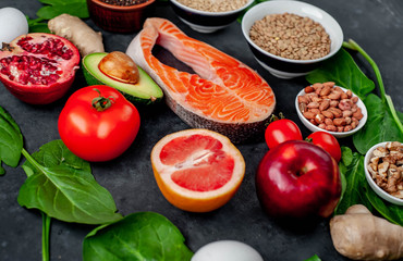 Selection of healthy food: salmon, fruits, seeds, cereals, superfoods, vegetables, leafy vegetables on a stone background. Healthy food for people.