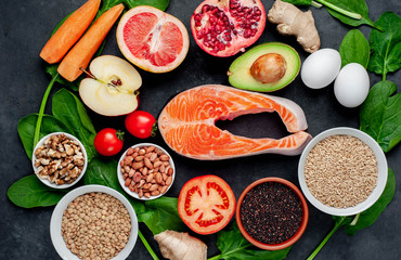 Selection of healthy food: salmon, fruits, seeds, cereals, superfoods, vegetables, leafy vegetables on a stone background. Healthy food for people.