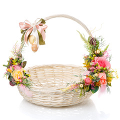 Fototapeta na wymiar White Easter basket with a bow on the handle and a variety of flowers. Decor in delicate pink and green colors.