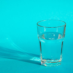 A glass with clean clear clear water stands on a blue background with green shadows. Clean water