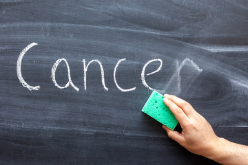 A hand erases the word CANCER from the chalkboard