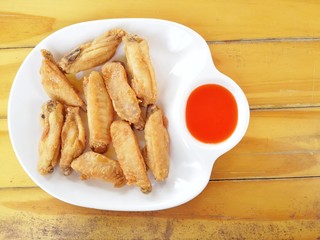 Fried chicken wings, placed in a white container There is a red tomato sauce, the wood floor is the background.