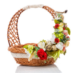 Fototapeta na wymiar Brown wicker basket with original handle. Decor with flowers, eggs and a small ceramic bird. Made in a rustic style.