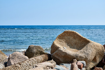 Fototapeta na wymiar Sinai Peninsula, a large boulder resembling an armchair, on the shores of the Red Sea, next to other stones, blue water and blue sky.