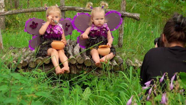Female photographer takes pictures of beautiful girls playing violet butterflies. Photoshoot of little girls wearing handmade butterfly wings