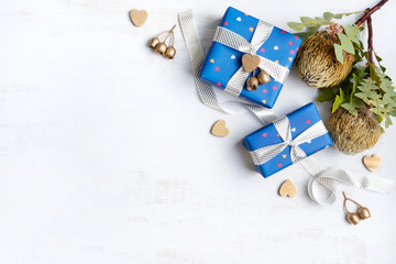 Fototapeta na wymiar Gifts wrapped in blue paper, tied with classic white & gold ribbon decorated by Australian Banksia, gold hearts & gold eucalyptus gum nuts. Gifts for Valentines day, Anniversary, birthday, mothers day