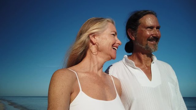 Mature man and woman walking together on a beach and both smiling and laughing.