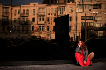 Beautiful redhead woman wearing red dress and stylish coat on city street. loneliness and depression concept.
