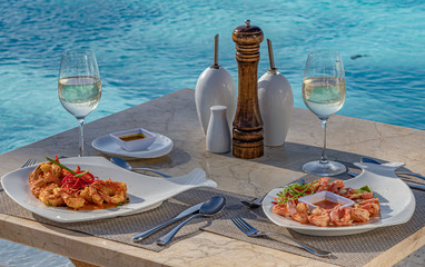 Two plates with shrimp starters, white wine, on a restaurant table