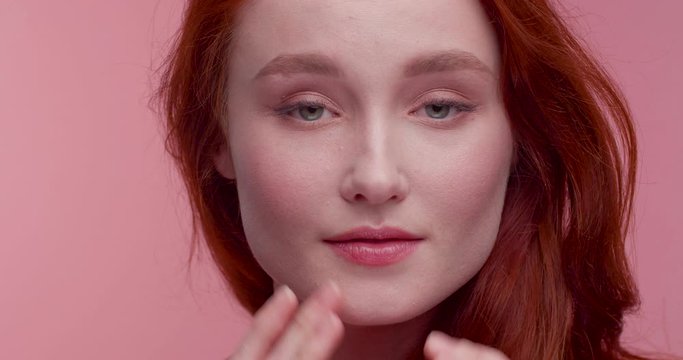 Pretty Ginger Woman touching her Face with her Fingers while posing on Camera and looking at Objective. Having nice Appearance and Charming smile. Looking gorgeous and having natural Beauty.