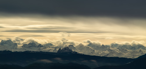 Dramatic landscape of snowy mountain tops in the Swiss alps as seen from the Zurich area late afternoon sun light illuminating from behind a thick sheet of clouds