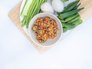 Top view or directly above of Thai chili sauce (Nam Prik) in the ceramic bowl with boilded eggs and vegatables on wooden cutting board and gray background.