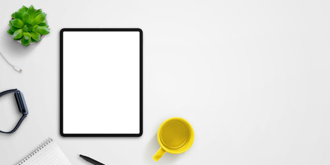 Tablet mockup on desk surrounded by watch, coffee mug, pad, plant and pen. Copy space beside for text