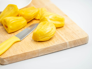 Closeup of yellow ripe jackfruit, knife, white ceramic dish on wooden cutting board in the kitchen or restaurant.